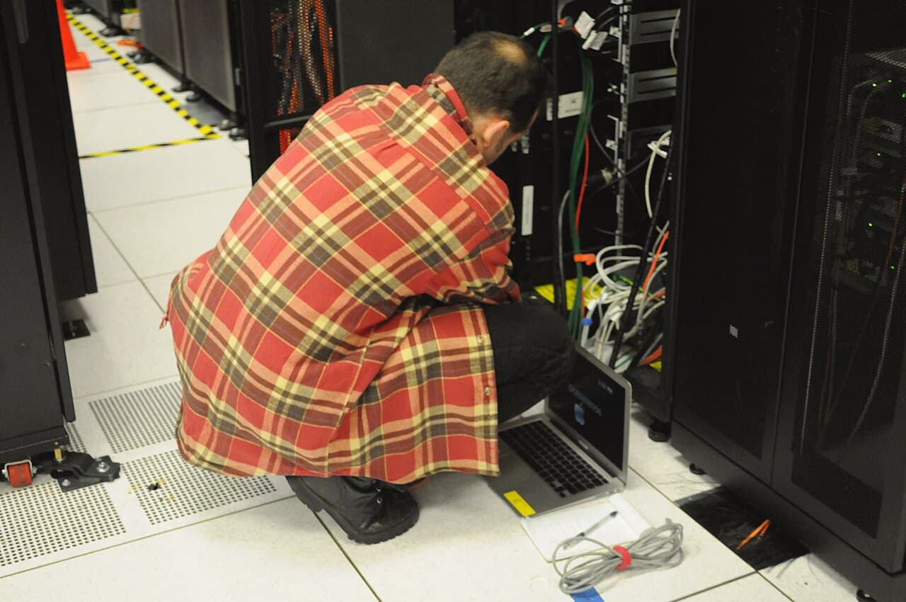 Technician with a laptop working on a server rack, illustrating the build versus buy decision for AI agents
